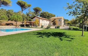 Una casa de dos pisos con piscina, rodeada por un césped cuidado y árboles.