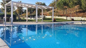 Una piscina cristalina con una estructura de pérgola, paredes de piedra y un jardín ajardinado.