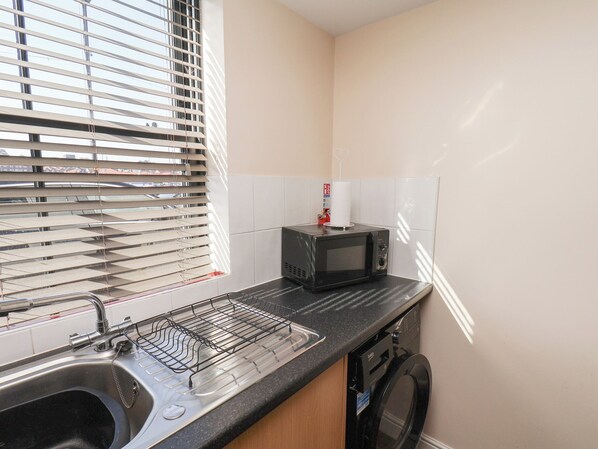 A kitchen with a sink, a microwave, a dish rack, and a washing machine. - Marina Side (Whitby)