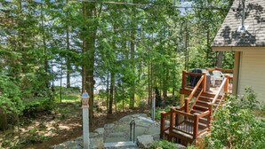 Eine Holztreppe führt zu einer Terrasse mit Blick auf einen Wald und ein Gewässer.