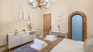 A bedroom with a bed, a chest of drawers, a vanity, a chandelier, and a brick archway.