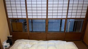 Una camera d'albergo con un tradizionale schermo giapponese shoji, due letti con biancheria bianca e un piccolo comodino con una lampada.