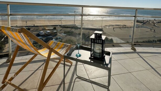 Ein Balkon mit Blick auf den Strand, ein Stuhl, ein Tisch mit einem Glas und eine Laterne.