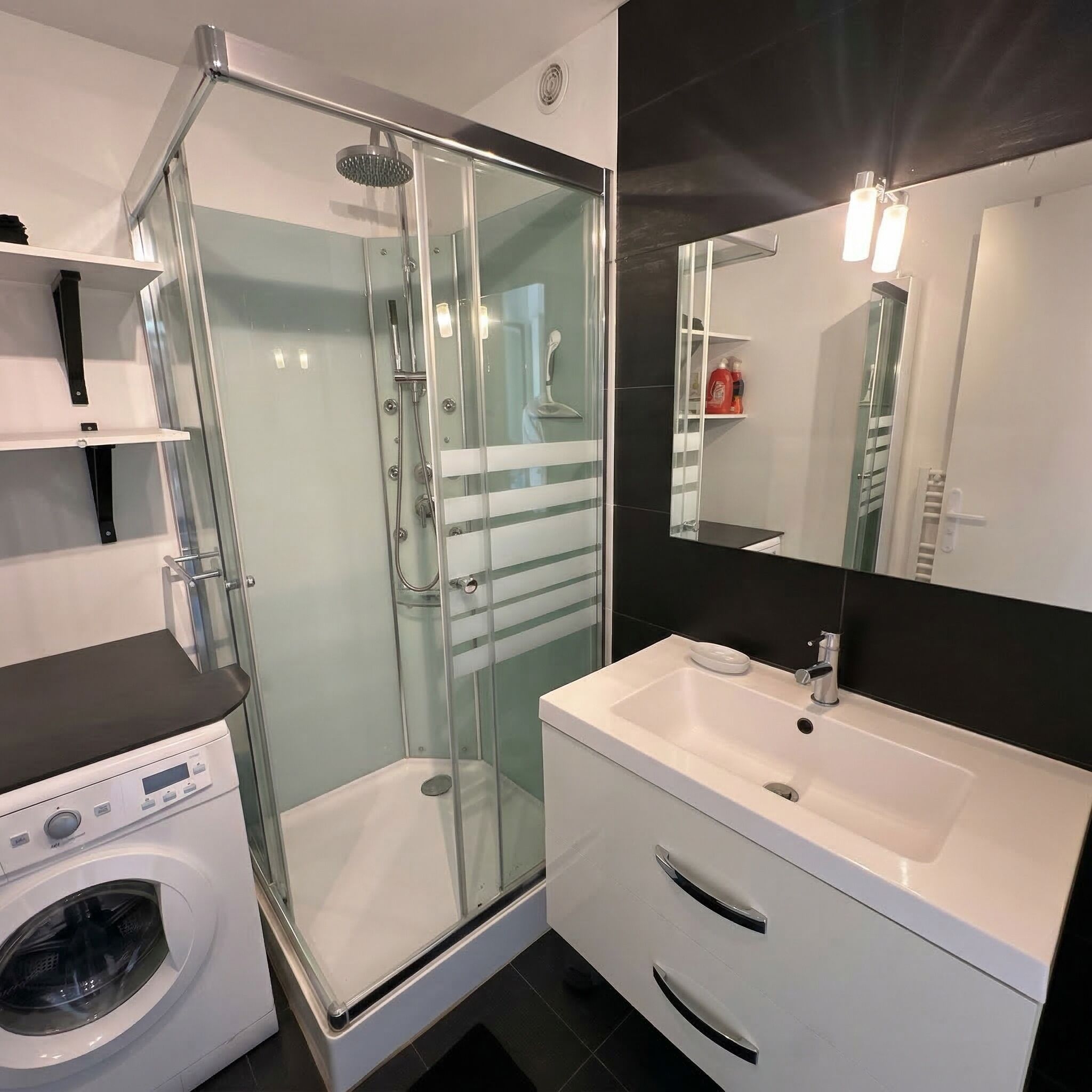 A modern bathroom with a glass-enclosed shower, a white sink, and a built-in washing machine.