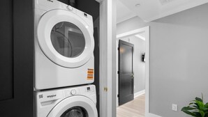 A laundry room with two Whirlpool washing machines, a dark door, and a hallway leading to another room.