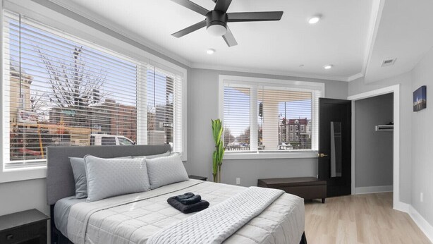 A bedroom with a bed, a ceiling fan, and large windows with blinds.