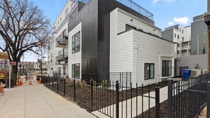 A modern multi-story residential building with balconies, a gated driveway, and a clear sky.