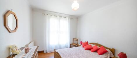 A bedroom with a wooden bed, a nightstand, a dresser, a mirror, and a window with curtains.