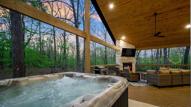 A hot tub in a wooden deck area with a stone fireplace and outdoor seating. - Pickleball, Pool, Splash Fountain ,Clubhouse , Walking Trails , Basketball (Broken Bow)