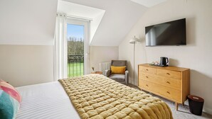 A bedroom with a bed, a dresser, a TV, and a window with a view of a garden. - MH Hôtel & Spa (Arradon)