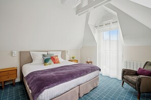 A bedroom with a bed, a nightstand, a chair, a window with curtains, and a radiator. - MH Hôtel & Spa (Arradon)