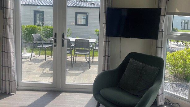 Una habitación con puerta de vidrio corrediza que da a un patio exterior, televisor de pantalla plana en la pared y un sillón verde.
