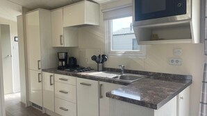 Una cocina moderna con armarios blancos, microondas integrado, cafetera y una ventana.