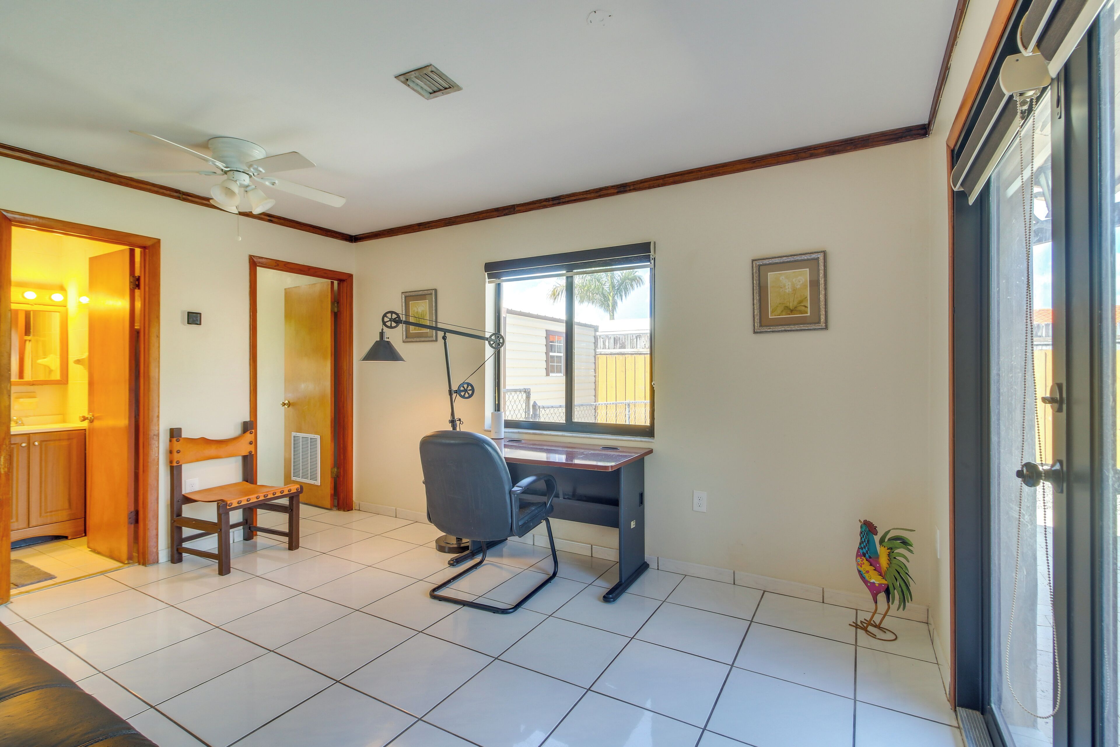 Una habitación con escritorio, silla, ventilador de techo y ventana con vistas.