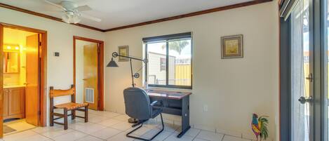 Una habitación con escritorio, silla, ventilador de techo y ventana con vistas.