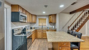 Une cuisine avec des meubles en bois, un plan de travail en granit, des appareils électroménagers en acier inoxydable et un escalier en bois.