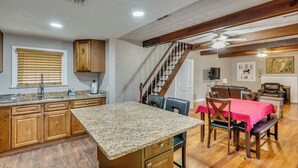 Une cuisine dotée de plans de travail en granit, de meubles en bois, d’un coin repas avec une nappe rouge et d’un escalier avec des rampes en bois.