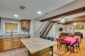 A kitchen with granite countertops, wooden cabinets, a dining area with a red tablecloth, and a staircase with wooden railings.