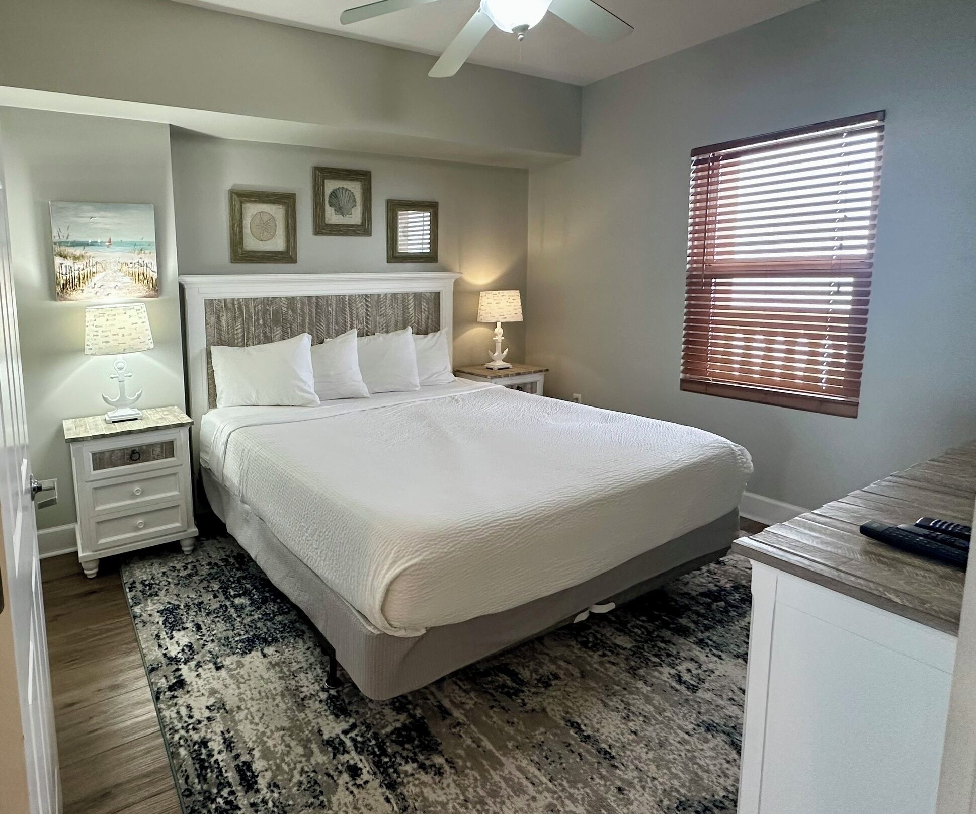 A bedroom with a bed, nightstands, a lamp, a window with blinds, and wall decorations.