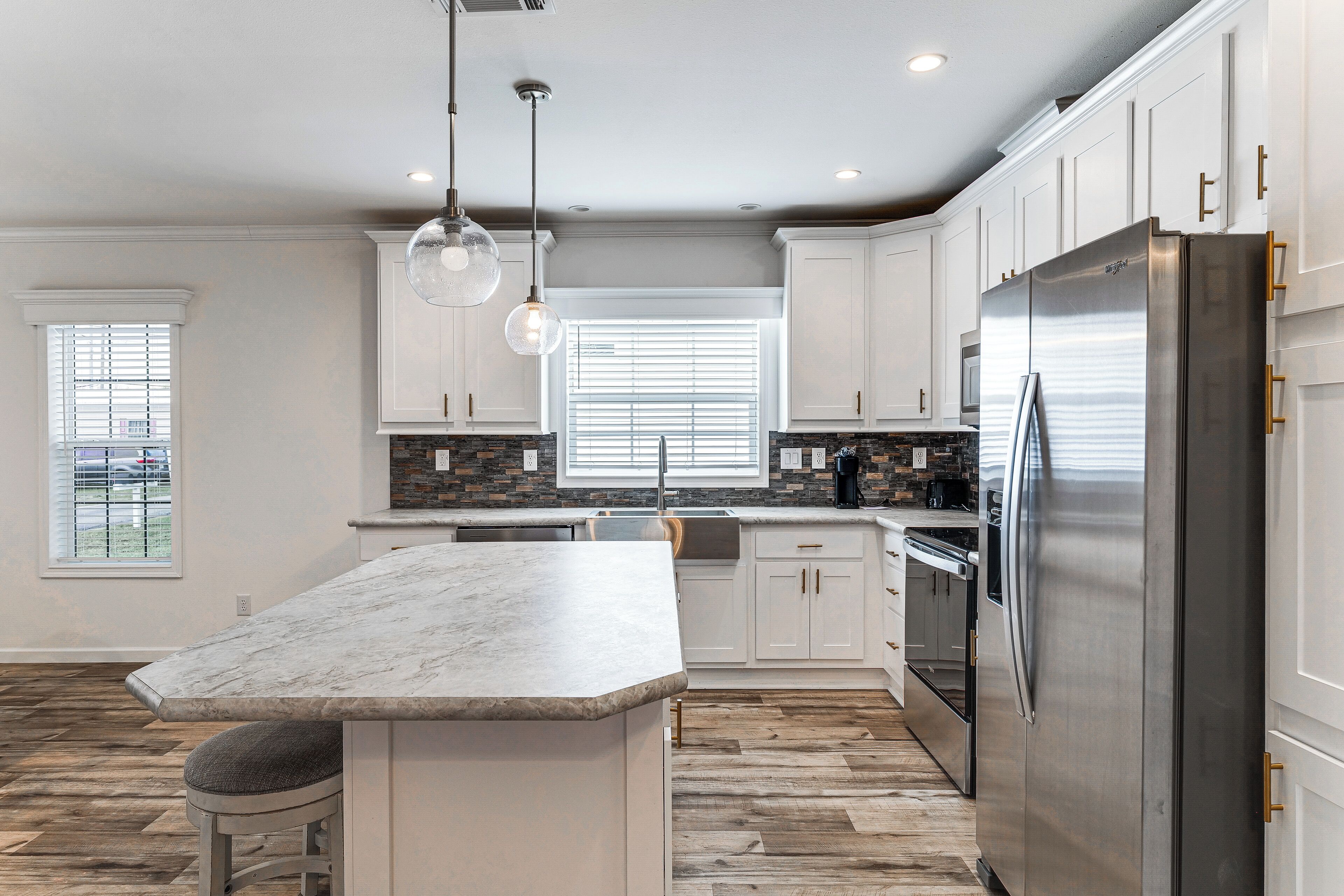 A kitchen with a large island, stainless steel refrigerator, and pendant lighting.