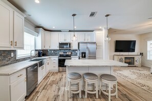 A modern kitchen with white cabinets, stainless steel appliances, a central island with stools, and a flat-screen TV. - 7 Mi to Disney: Family Home w/ Heated Pool Access (Davenport)
