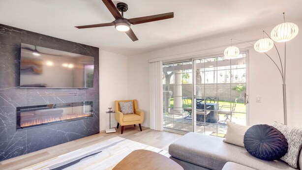 A modern living room with a fireplace, a ceiling fan, a sofa, and a dining area. - Patio & Pool Access! Mtn-view Palm Springs Escape (Palm Springs)