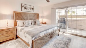 A bedroom with a wooden bed, a ceiling fan, a large window, and a nightstand with a lamp. - Patio & Pool Access! Mtn-view Palm Springs Escape (Palm Springs)