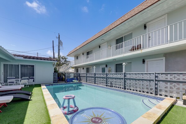A swimming pool with a sun design, a white building with a balcony, and a green lawn area. - Dog-friendly Unit w/ Pool Access in Pompano Beach! (Pompano Beach)