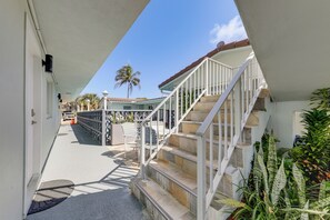 Ein Korridor mit einer Treppe, die zu einem Balkon führt, einer Palme und Blick auf ein Gebäude mit rotem Dach.