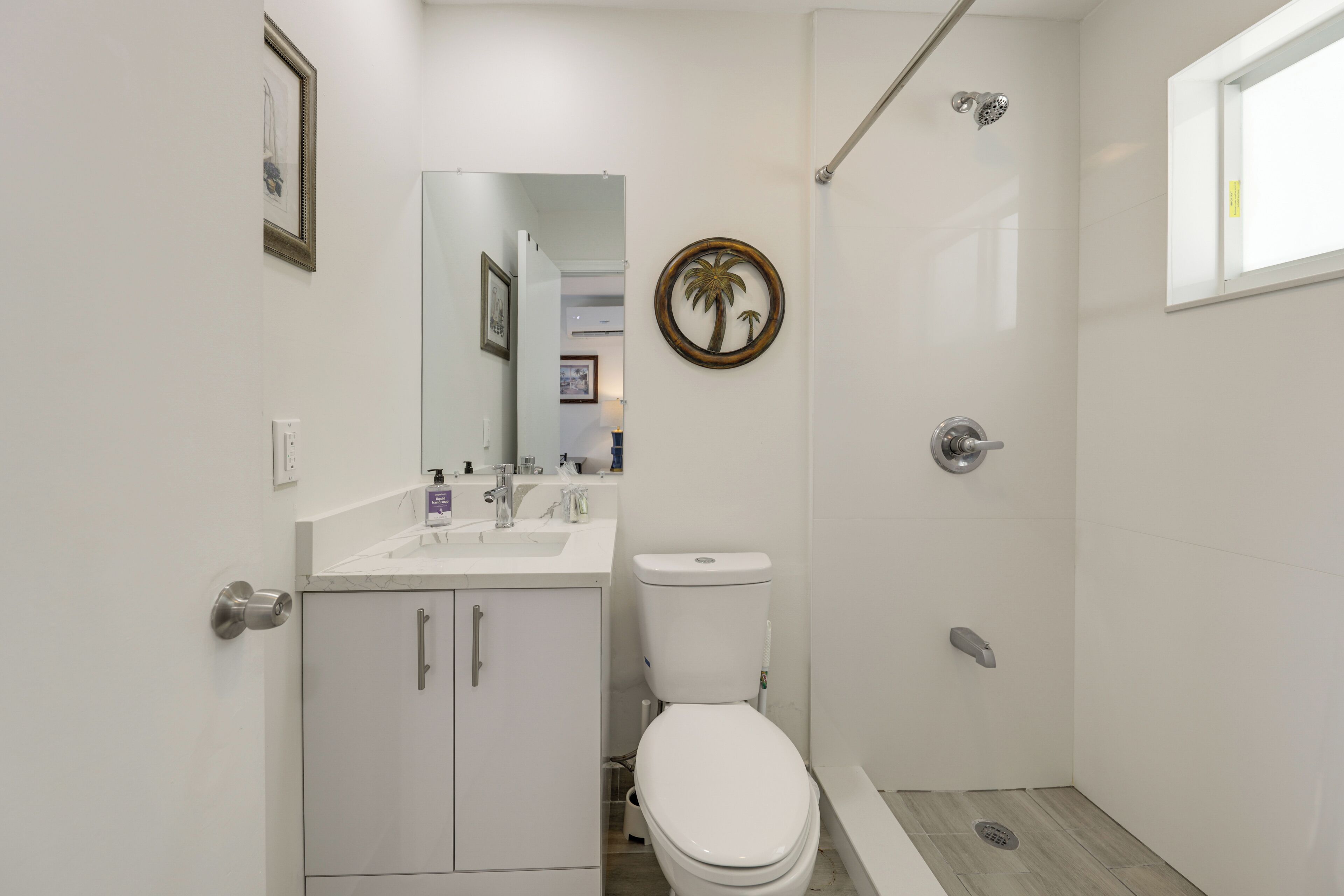 A bathroom with a toilet, sink, mirror, shower, and a framed picture on the wall.