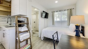 Ein Schlafzimmer mit Bett, Fernseher, Nachttisch mit Lampe, einer Holzlade mit Handtüchern, einer Dusche und einem Badezimmer mit Waschbecken und Toilette.