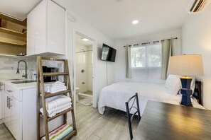 Ein Schlafzimmer mit Bett, Fernseher, Nachttisch mit Lampe, einer Holzlade mit Handtüchern, einer Dusche und einem Badezimmer mit Waschbecken und Toilette.