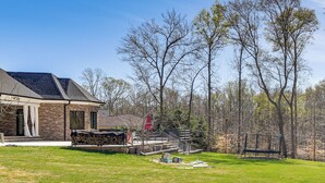 A house with a stone exterior, a covered patio, and a fenced yard with trees. - Luxe Extended Stay w/ Swim Spa in Indian Land! (Fort Mill)