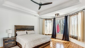A bedroom with a wooden bed, a nightstand, a ceiling fan, and a window with curtains. - Luxe Extended Stay w/ Swim Spa in Indian Land! (Fort Mill)