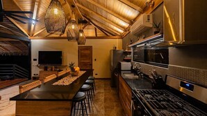Une cuisine dotée d’un grand îlot central, de tabourets de bar, de luminaires suspendus et d’un téléviseur.