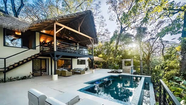 Une maison moderne dotée d’une piscine, d’un espace salon extérieur et d’une structure à toit de chaume.