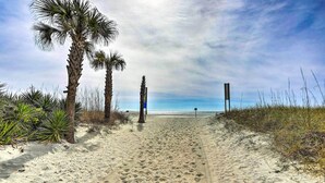 Un sendero arenoso en la playa, con palmeras y una estructura de madera al fondo.
