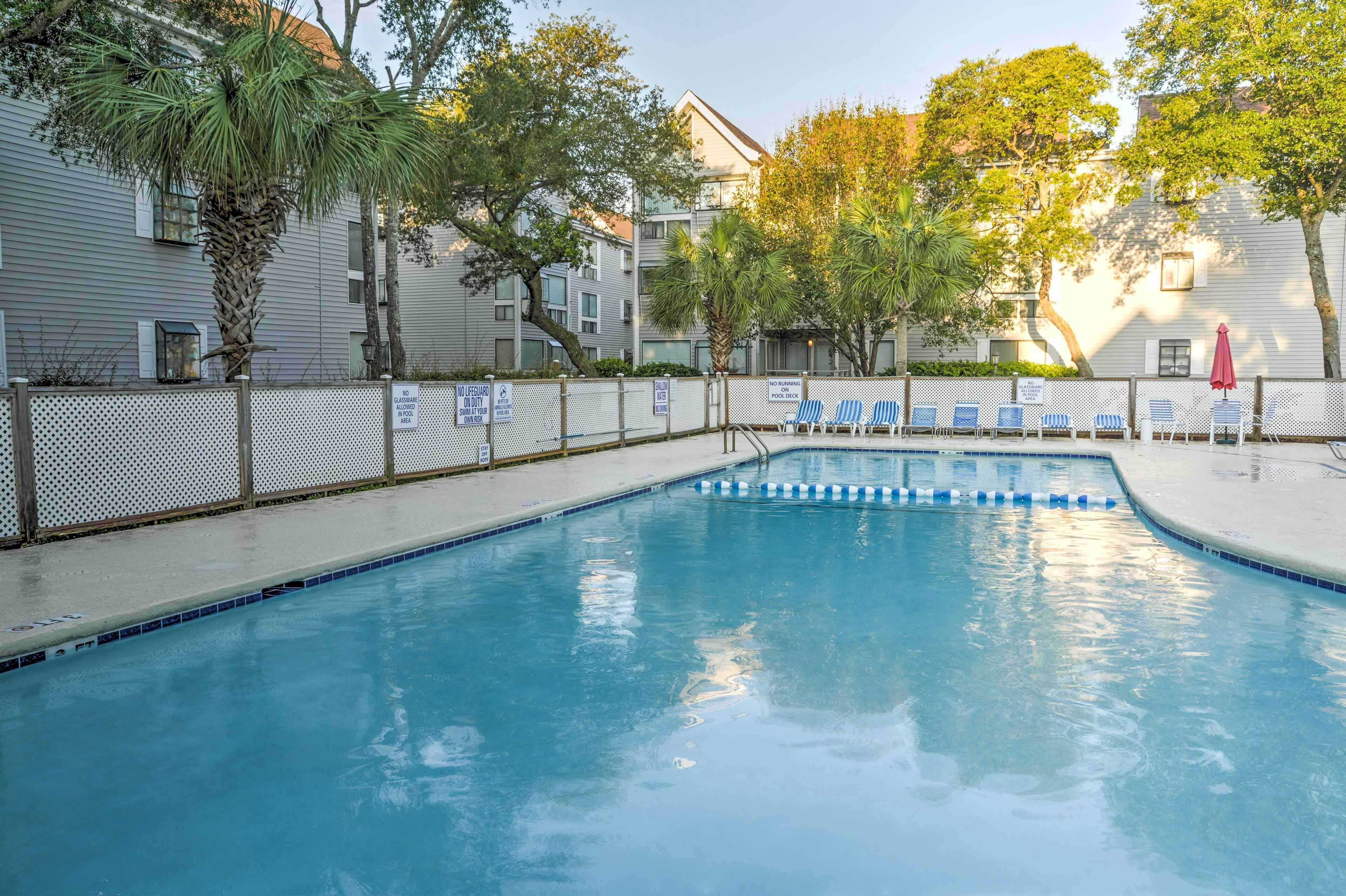 Una piscina con confini blu e bianchi, circondata da una recinzione con palme e un edificio sullo sfondo.
