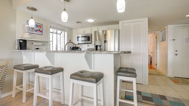 Una cocina con armarios blancos, un microondas, un refrigerador y dos taburetes de bar con asientos acolchados.