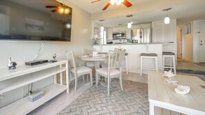 Una cocina moderna con armarios blancos, un microondas y un ventilador de techo. Hay un comedor con sillas blancas y una mesa.