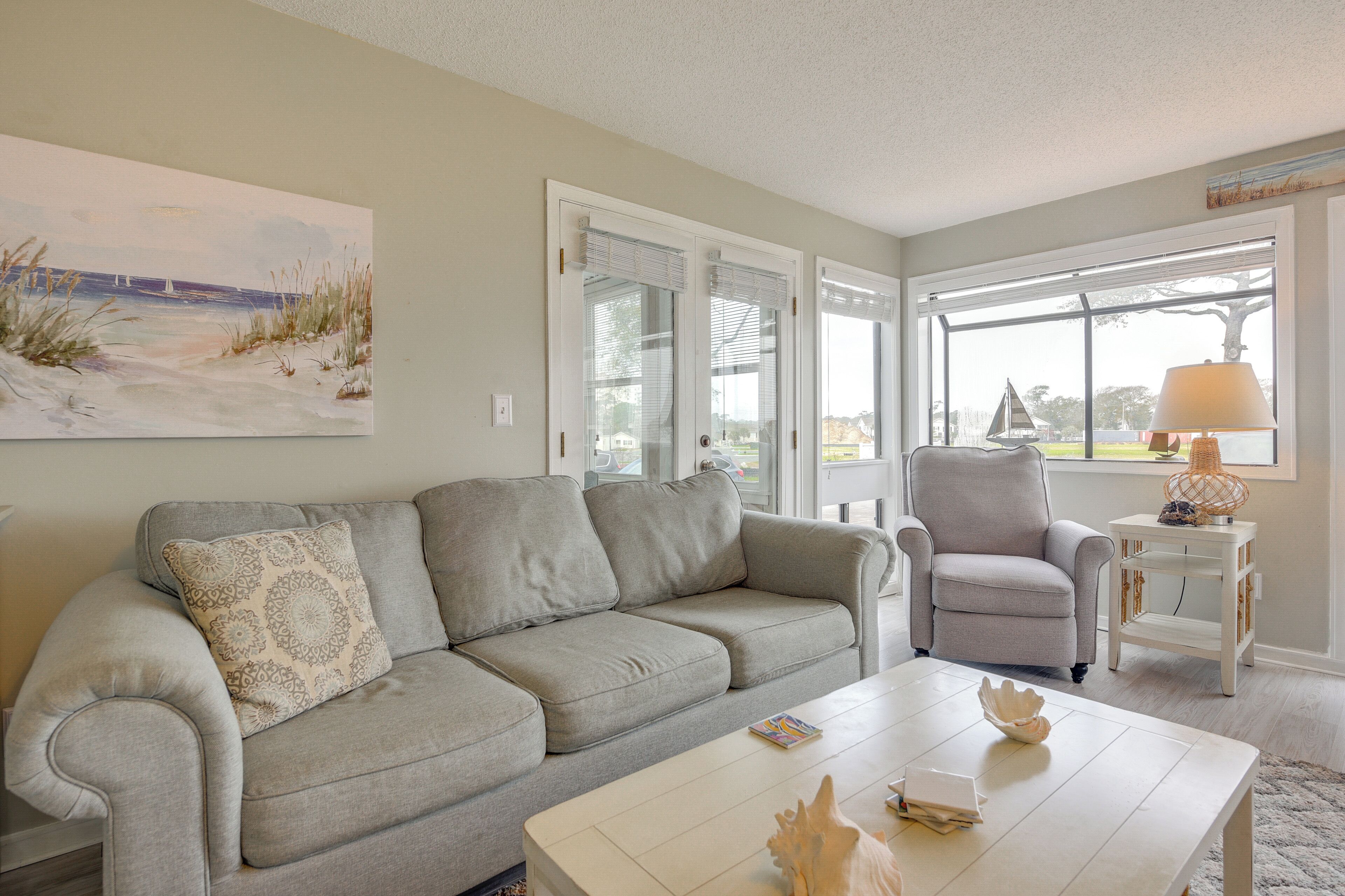 A living room with a gray sofa, a white coffee table, a side table with a lamp, and a painting of a beach scene.