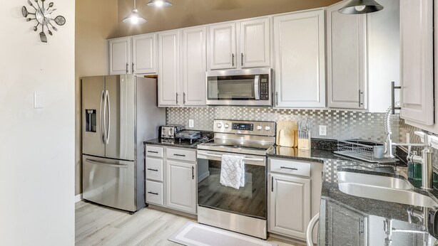 A modern kitchen with stainless steel appliances, white cabinets, and a tiled backsplash. - Private Yard & Patio: Spacious Retreat in Omaha! (Omaha)