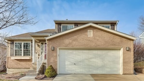 A two-story house with a garage, a front porch, and a small front yard. - Private Yard & Patio: Spacious Retreat in Omaha! (Omaha)
