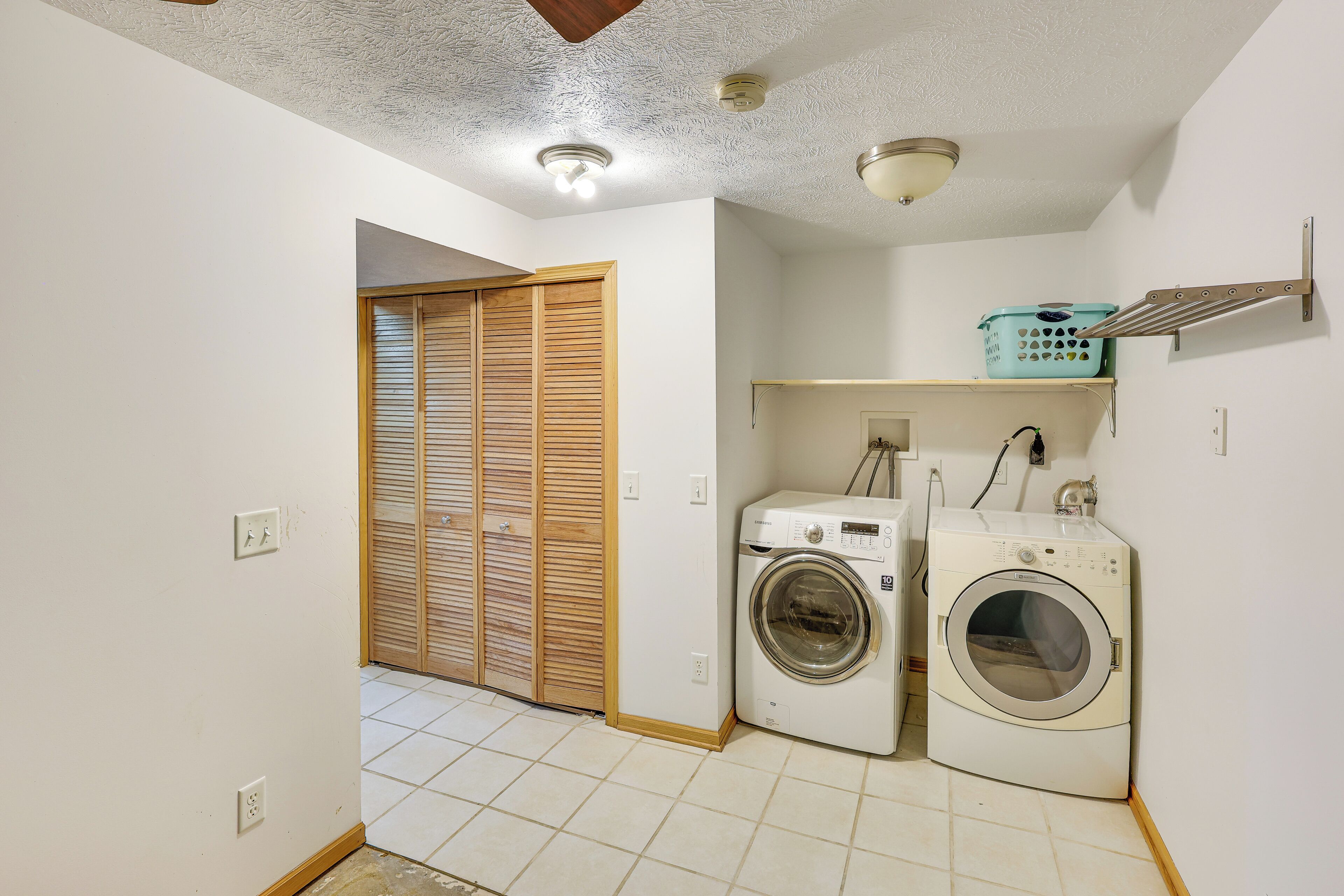 A laundry room with a washing machine, dryer, and a shelf with a laundry basket.