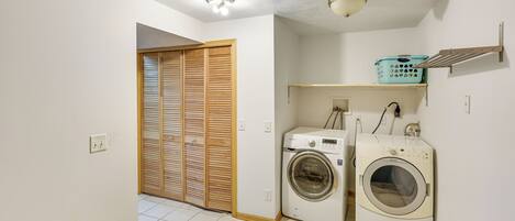 A laundry room with a washing machine, dryer, and a shelf with a laundry basket.