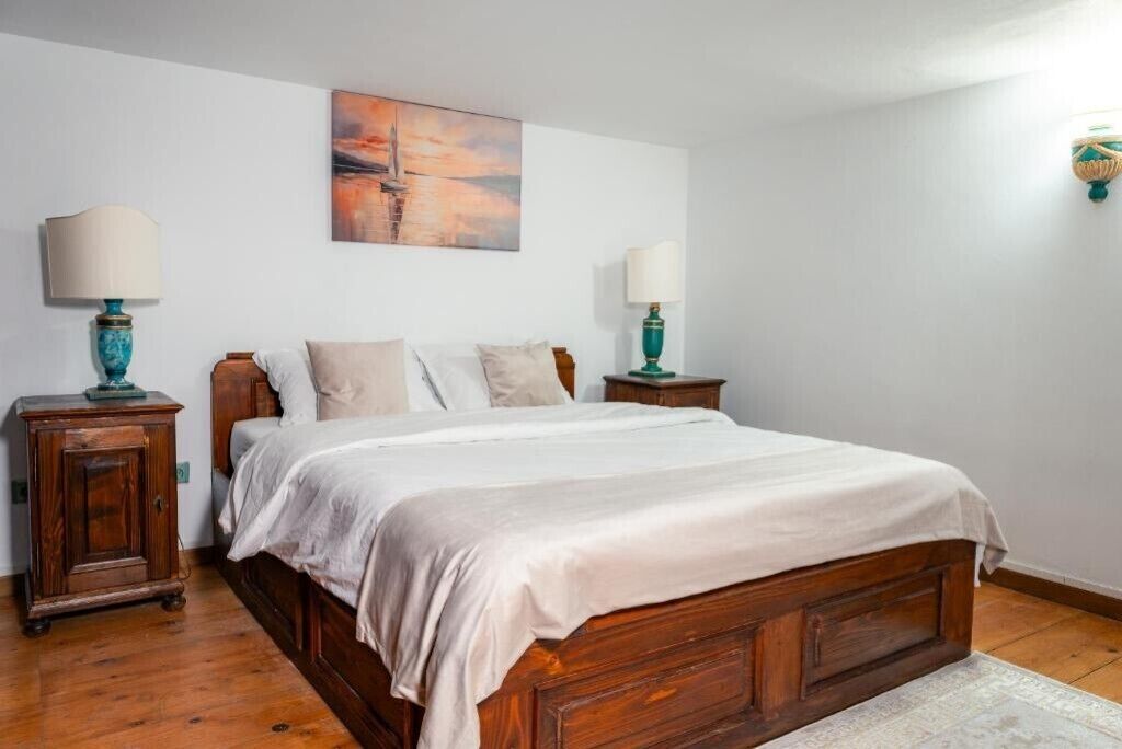 A bedroom with a wooden bed, two bedside tables with lamps, a painting on the wall, and a wooden cabinet.