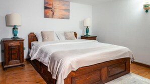 Een slaapkamer met een houten bed, twee nachtkastjes met lampen, een schilderij aan de muur en een houten kast.