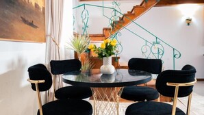 Een eetgedeelte met een ronde tafel, zwarte stoelen en een vaas met gele bloemen.