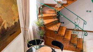 Een houten trap met groene metalen leuning, een ronde tafel met stoelen en een potplant.