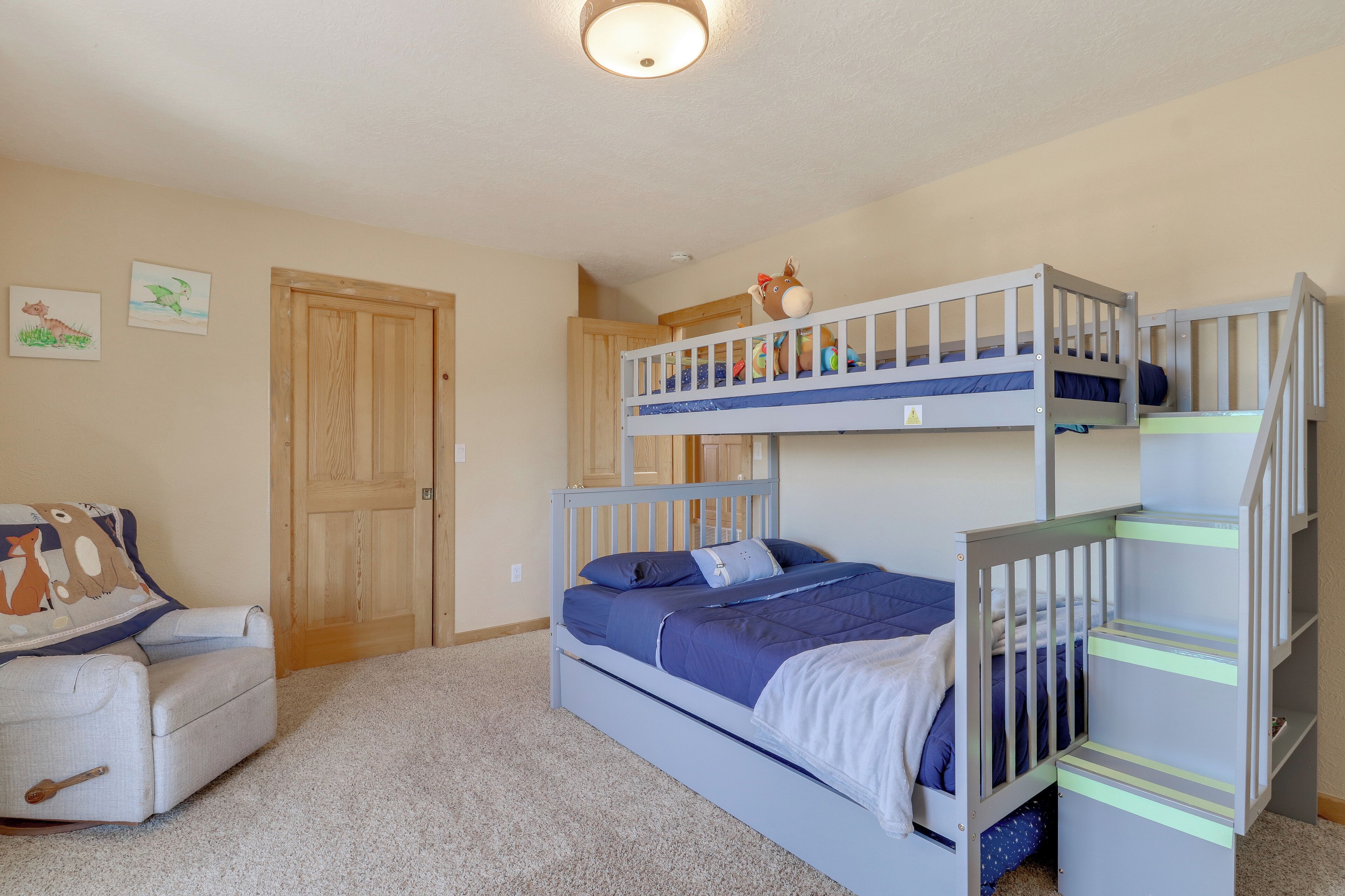 Une chambre avec un lit superposé, une porte en bois, une petite chaise et un sol recouvert de moquette.